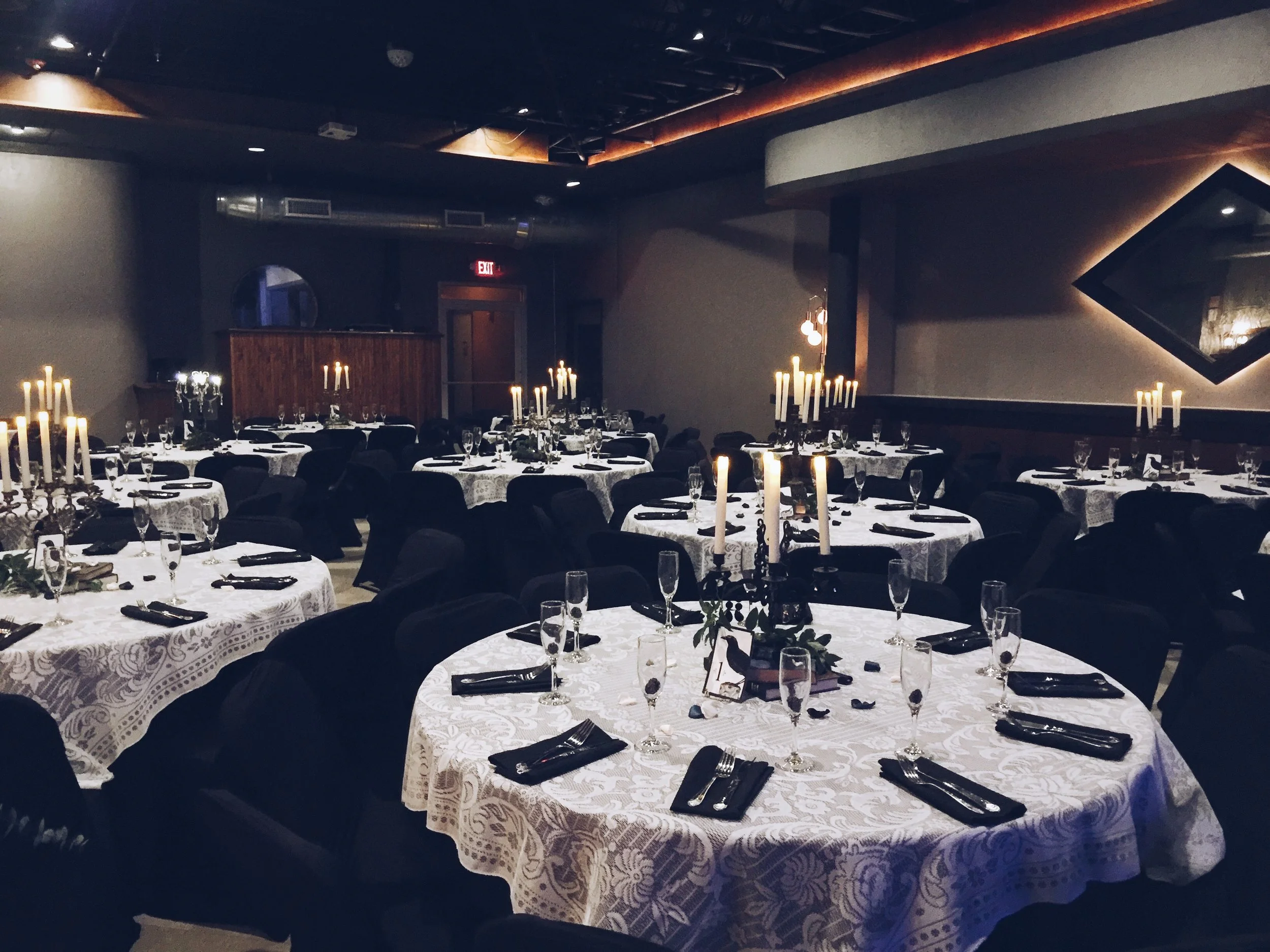 Atmospheric interior photograph of the venue during an evening gathering, soft candlelight on round tables, dark linen, glassware reflecting warm tones, moody and intimate.